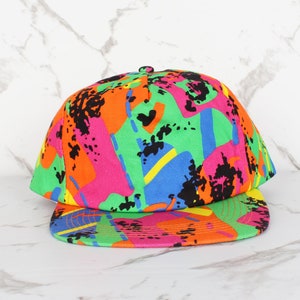 Op de afbeelding: Een kleurrijke baseballpet met een abstract patroon in groen, oranje, roze, blauw en zwart.