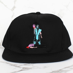 May include: Black and blue embroidered baseball cap with a video game character graphic. The character is wearing a blue and white outfit and is holding a pink fist.