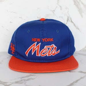 Puede incluir: Una gorra de béisbol azul y naranja con el texto "NEW YORK Mets" bordado en rojo en la parte delantera.