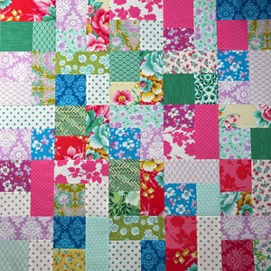 May include: A patchwork quilt featuring a variety of floral and patterned fabrics in a vibrant array of colors. The quilt is composed of numerous squares and rectangles, showcasing a mix of pinks, blues, greens, and reds. The design includes polka dots, floral prints, and geometric patterns.