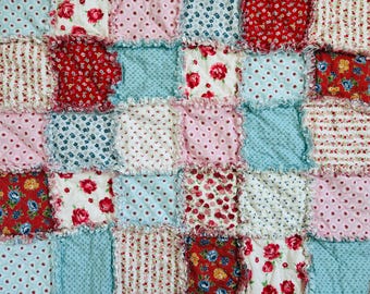 Peut inclure: Une courtepointe en patchwork composée de divers carrés de tissu aux bords effilochés. Les motifs incluent des roses rouges sur fond blanc, des pois bleus et roses, de petites fleurs et des rayures dans des tons de rouge, bleu, rose et blanc.