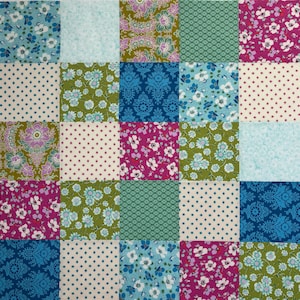 May include: A patchwork quilt square featuring a grid of 25 fabric squares. Each square displays a unique floral, polka dot, or patterned design in shades of blue, green, pink, and cream. The quilt is likely handmade.