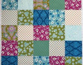 Peut inclure: Un carré de patchwork avec une grille de 25 carrés de tissu. Chaque carré présente un motif floral, à pois ou à motifs unique dans des tons de bleu, vert, rose et crème. La courtepointe est probablement faite à la main.