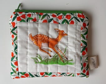 Peut inclure: Une pochette matelassée avec une illustration de faon courant sur fond blanc. La pochette est dotée d'une fermeture éclair verte et bordée d'un motif floral rouge et vert. Une petite étiquette avec les initiales "SBJ" est attachée.