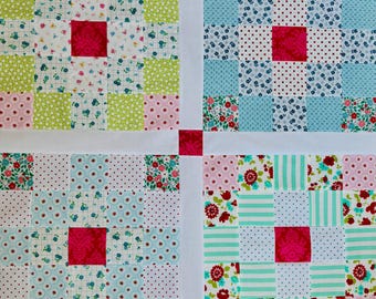 Peut inclure: Un dessus de courtepointe en patchwork composé de quatre blocs carrés distincts séparés par des bandes blanches et un carré rouge central. Chaque bloc est formé d'une grille de petits carrés de tissu aux motifs floraux, à pois et rayés dans des tons de rose, vert, bleu et blanc, avec un carré rouge uni au centre.