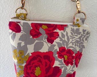 Peut inclure: Petit sac à bandoulière à motifs floraux avec un fond crème, des fleurs rouges, des feuilles grises et des accents jaunes. Le sac a une fermeture éclair et une quincaillerie dorées, et une sangle à motifs noir et blanc.