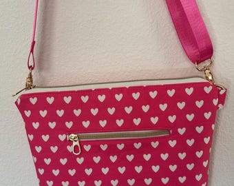 Peut inclure: Sac bandoulière rose orné de cœurs blancs. Il est doté d'une fermeture éclair dorée et d'une bandoulière rose assortie. Fabriqué en tissu résistant, il est idéal pour un usage quotidien. Il comprend une poche zippée au dos.