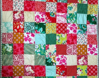 Peut inclure: Une courtepointe patchwork avec une variété de tissus à motifs floraux et autres, dans des tons de rouge, rose, vert et crème. La courtepointe est composée de nombreux carrés, chacun avec un motif différent, bordés d'un tissu rayé vert clair et blanc.