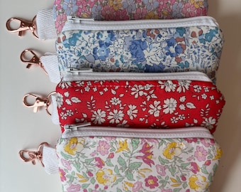 Peut inclure: Quatre pochettes rectangulaires en tissu avec des motifs floraux dans des tons rose, bleu, rouge et multicolore. Chaque pochette dispose d'une fermeture éclair blanche, d'une languette en tissu blanc et d'un mousqueton en métal or rose.