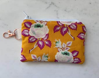 Peut inclure: Petite pochette zippée jaune moutarde ornée d'un motif floral avec des roses blanches et roses et des feuilles violettes. La pochette a une fermeture éclair bleu clair et un fermoir or rose attaché à une sangle crème. Environ 12 cm de large.