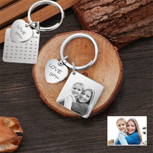 May include: Silver keyring with a calendar charm, two heart charms with the text "Love you" on each, and a square charm with a black and white photo of two people. The calendar charm has the numbers 1 through 31 on it.