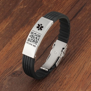 Puede incluir: Una pulsera de silicona negra con un cierre de metal plateado y una placa plateada con el texto "HEALTH INFO" y un código QR que dice "SCAN ME".