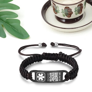 May include: Black medical alert bracelet with a braided cord and a stainless steel tag. The tag has a star of life symbol, the words "HEALTH INFO" and "SCAN ME", and a QR code.