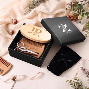 May include: A black gift box containing a wooden beard brush with the initials "JR" and the name "Jeremiah", a wooden comb, and small scissors. The box also includes a black velvet pouch. The box lid has the name "Nicholas".