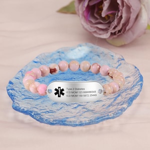 Puede incluir: Un brazalete de cuentas rosadas con una etiqueta de alerta médica plateada que dice "Type 2 Diabetes, ICD MOM 123 666686548, ICD MOM 159 5872 25449".