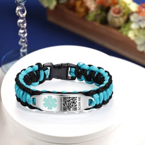 May include: A black and turquoise paracord bracelet with a silver medical ID tag. The tag has a red star of life symbol, a QR code, and the text "HEALTH INFO SCAN ME".