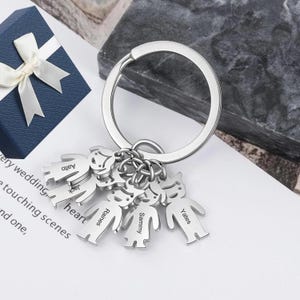 Peut inclure: Porte-clés en argent avec six petits charms en forme de personnes. Chaque charme porte un nom différent gravé dessus : Alito, Jack, Princess, Sammy, Yates.