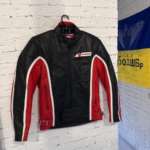 May include: Black leather motorcycle jacket with red and white accents. The jacket features a zip-up front, a small logo on the chest, and a buckled waist. The sleeves have white stripes and red panels.
