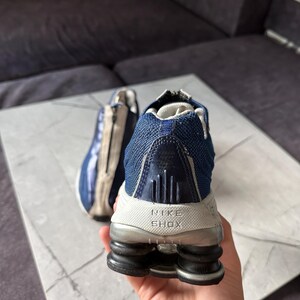 May include: A pair of Nike Shox athletic shoes. The shoes are primarily navy blue and white, with a mesh upper and a distinctive Shox sole. The Nike Shox logo is visible on the heel.