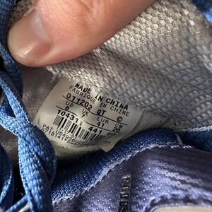 May include: Close-up of the inside of a blue and white Nike sneaker. The label reads "MADE IN CHINA" with size information: US 8, UK 7, EUR 41, and CM 26. The shoe's interior is a textured gray fabric.