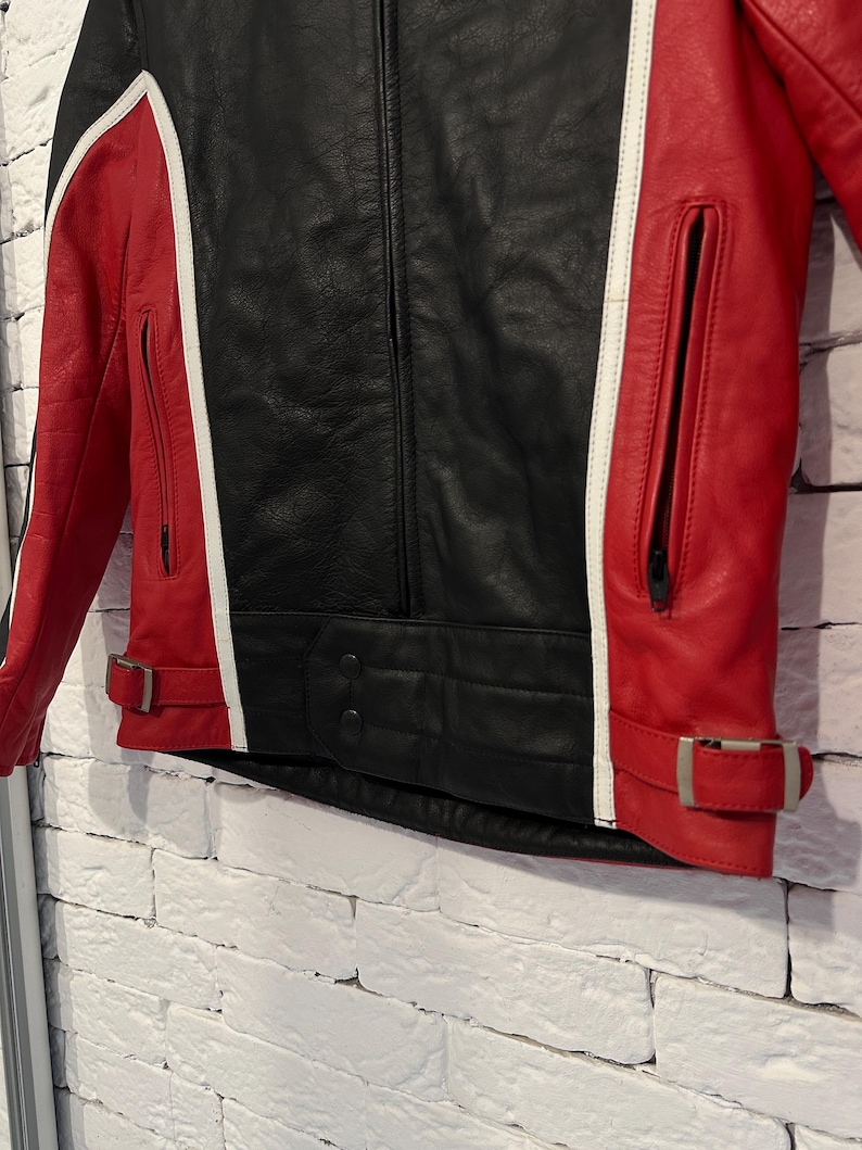 May include: Black and red leather jacket with white accents. The jacket features a central black panel, red side panels, and white stripes. It has a zippered front, pockets, and adjustable waist straps.
