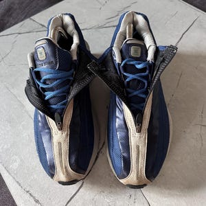 May include: Pair of blue and beige athletic shoes with a zipper closure. The shoes have blue laces and a mesh upper. The tongue and inner lining are gray. The soles are white and beige.