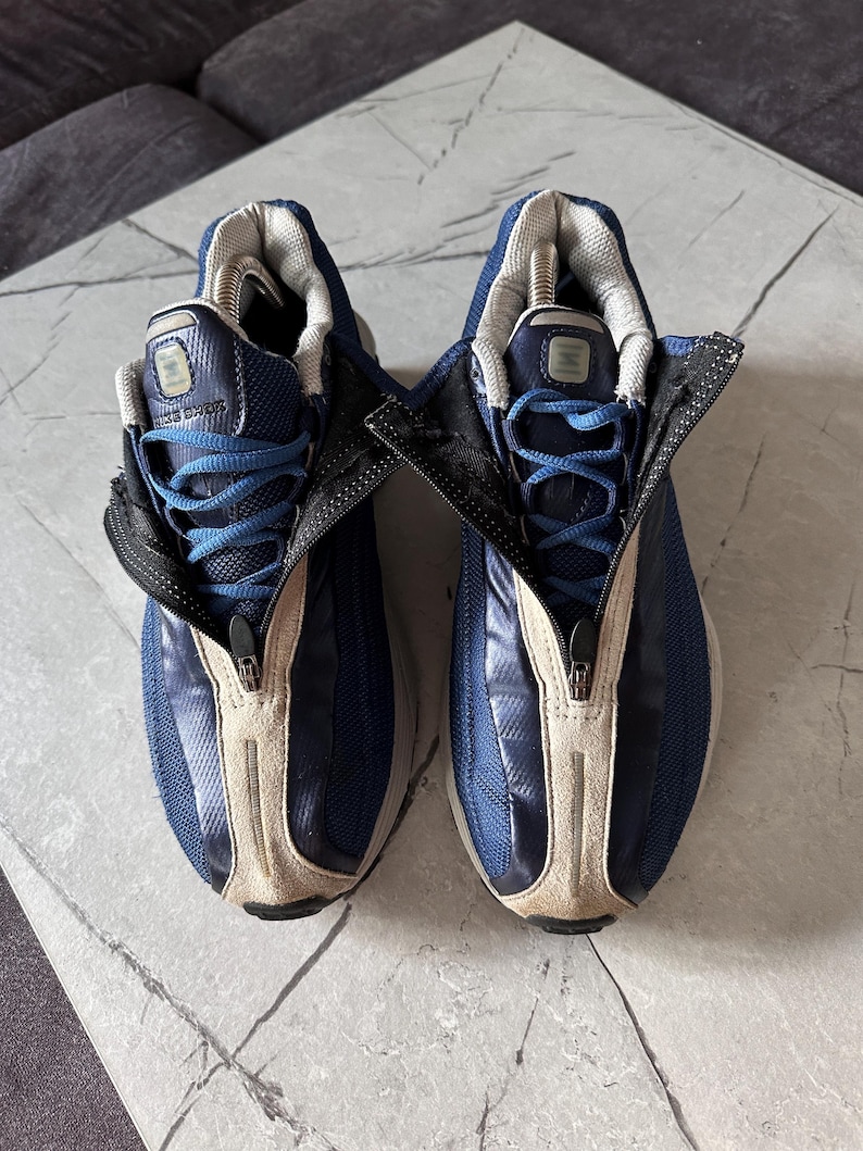 May include: Pair of blue and beige athletic shoes with a zipper closure. The shoes have blue laces and a mesh upper. The tongue and inner lining are gray. The soles are white and beige.