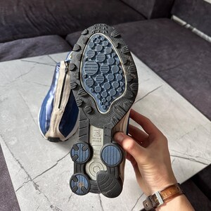 May include: A pair of blue and beige athletic shoes with a black and blue sole. The sole features a textured design with circular and oval patterns. The shoe has a zipper on the side and the brand name "Nike Shox" is visible.