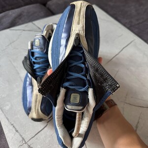 May include: Pair of blue and beige athletic shoes with a zipper closure. The shoes have blue laces and a beige suede-like material on the upper. The zipper reveals the laces and tongue. The shoes are on a marble surface.