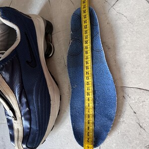 May include: A blue and white athletic shoe next to a blue insole being measured with a yellow tape measure. The insole measures approximately 10.5 inches in length.