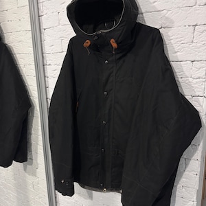 May include: A black hooded jacket featuring a front button closure, long sleeves, and brown leather toggles on the hood drawstrings. The jacket has a structured collar, a visible interior lining, and a clean, solid-colored exterior design.