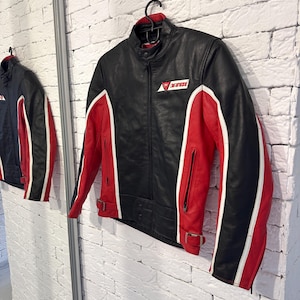 May include: Black and red leather motorcycle jacket with white accents. The jacket features a stand-up collar, zippered pockets, and a logo on the chest. The sleeves and sides are red with white stripes.