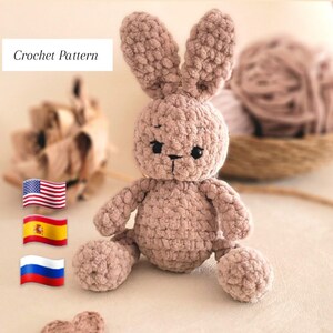 Puede incluir: Patrón de crochet para un conejito de peluche marrón claro. El conejito tiene una textura esponjosa y ojos negros. El patrón está disponible en inglés, español y ruso.
