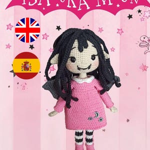 Puede incluir: Una muñeca de crochet con pelo negro, vestido rosa y leggings a rayas blancas y negras. La muñeca tiene una sonrisa amigable y lleva zapatos rosas. La muñeca está de pie frente a un fondo rosa con estrellas y un murciélago con el texto "ISADORA MOON" en él.