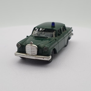 May include: A green toy car with a blue light on top. The car has a silver grill and headlights. It is a model of a classic Mercedes-Benz.