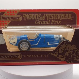 Può includere: Un'auto giocattolo blu Matchbox Models of Yesteryear Grand Prix, una Bugatti Type 51 del 1932, in una scatola rossa e marrone con il logo Matchbox. L'auto ha il numero 4 sul lato.