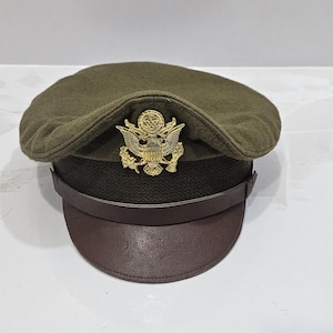 May include: A green military-style hat with a brown leather band and a gold eagle insignia.
