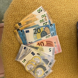May include: A stack of Euro banknotes in denominations of 5, 10, 20, and 50, with a few Euro coins on top. The banknotes are arranged in a fan shape, with the highest denomination at the top.