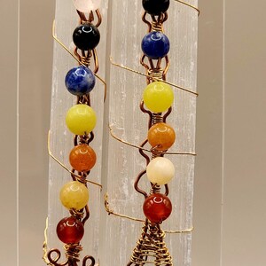 May include: Two selenite wands with copper wire wrapped around them. Each wand has seven beads of different colors: pink, black, blue, yellow, orange, white, and red.