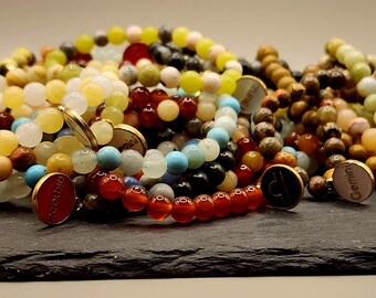 May include: A collection of colorful beaded bracelets with gold charms featuring zodiac signs, including Gemini, Libra, and Capricorn. The bracelets are made with various stones, such as turquoise, jade, and carnelian.