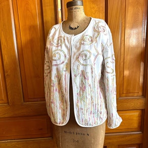 May include: White cotton jacket with a colorful embroidered design. The embroidery features swirls and lines in shades of pink, green, and yellow.