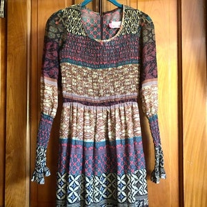 May include: A long-sleeved dress with a colorful patchwork design. The dress has a round neckline and a gathered waist. The fabric is a lightweight, sheer material.