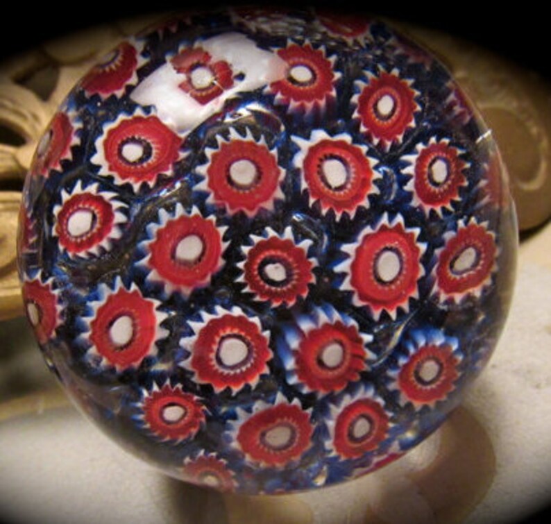 May include: A glass paperweight with a swirling pattern of red, white, and blue. The paperweight is round and has a smooth, glossy finish.