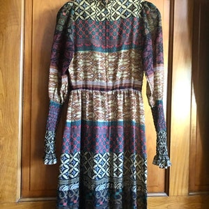 May include: A long-sleeved dress with a colorful, geometric pattern. The dress has a fitted bodice and a flowing skirt. The fabric is sheer and lightweight.