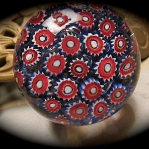 May include: A glass paperweight with a red, white, and blue pattern. The pattern is made up of small, circular designs.