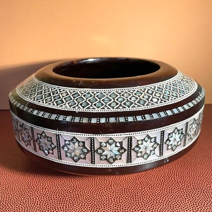 May include: A round wooden bowl with intricate inlaid mother-of-pearl designs. The bowl has a dark brown wood base and a white and silver inlay pattern.