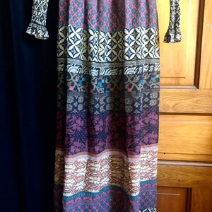 May include: A long, flowing maxi dress with a colorful, geometric pattern. The dress has a fitted bodice and a flowing skirt with a variety of colors, including brown, blue, red, and white.