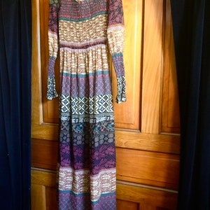 May include: A long-sleeved maxi dress with a colorful geometric pattern in shades of brown, red, blue, and white. The dress has a gathered waist and a flowing skirt.