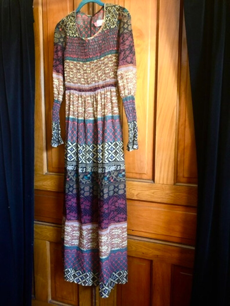 May include: A long-sleeved maxi dress with a colorful geometric pattern in shades of brown, red, blue, and white. The dress has a gathered waist and a flowing skirt.