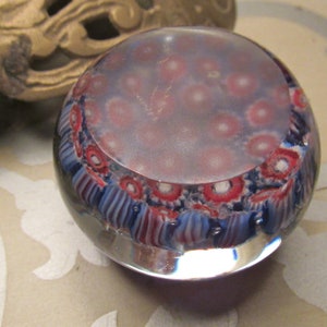 May include: A round glass paperweight with a swirling pattern of blue, red, and white. The paperweight has a clear glass base and a cloudy, white center.